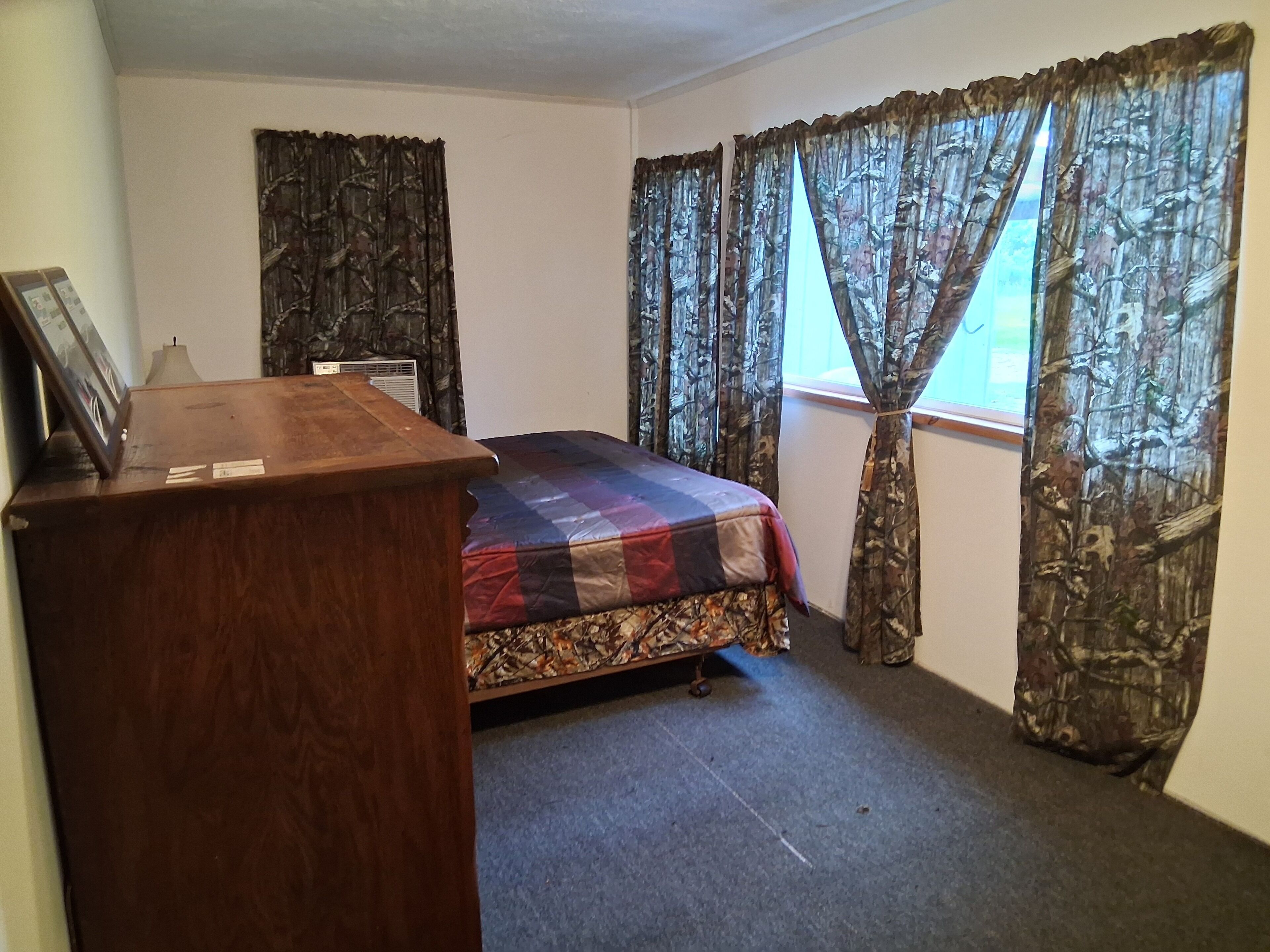 Une chambre à coucher avec un lit, un bureau en bois et des rideaux à motifs camouflage.
