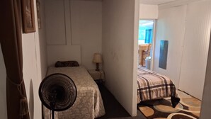 Ett sovrum med en säng, ett nattduksbord med en lampa, en golvfläkt och en mönstrad matta.