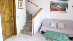 Una escalera con barandilla de madera, un sofá gris con dos cojines y una mesa tejida de color verde.