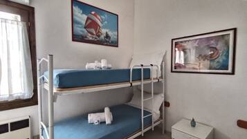 Een slaapkamer met stapelbed, een raam, een schilderij van een zeilboot en een klein nachtkastje.