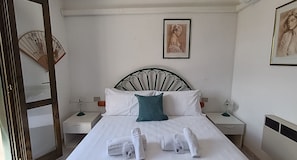Ein ordentlich bezogenes Bett mit weißen Leinen und einem türkisfarbenen Kissen, zwei Nachttische mit Lampen, ein gerahmtes Bild an der Wand und ein traditioneller Fächer.
