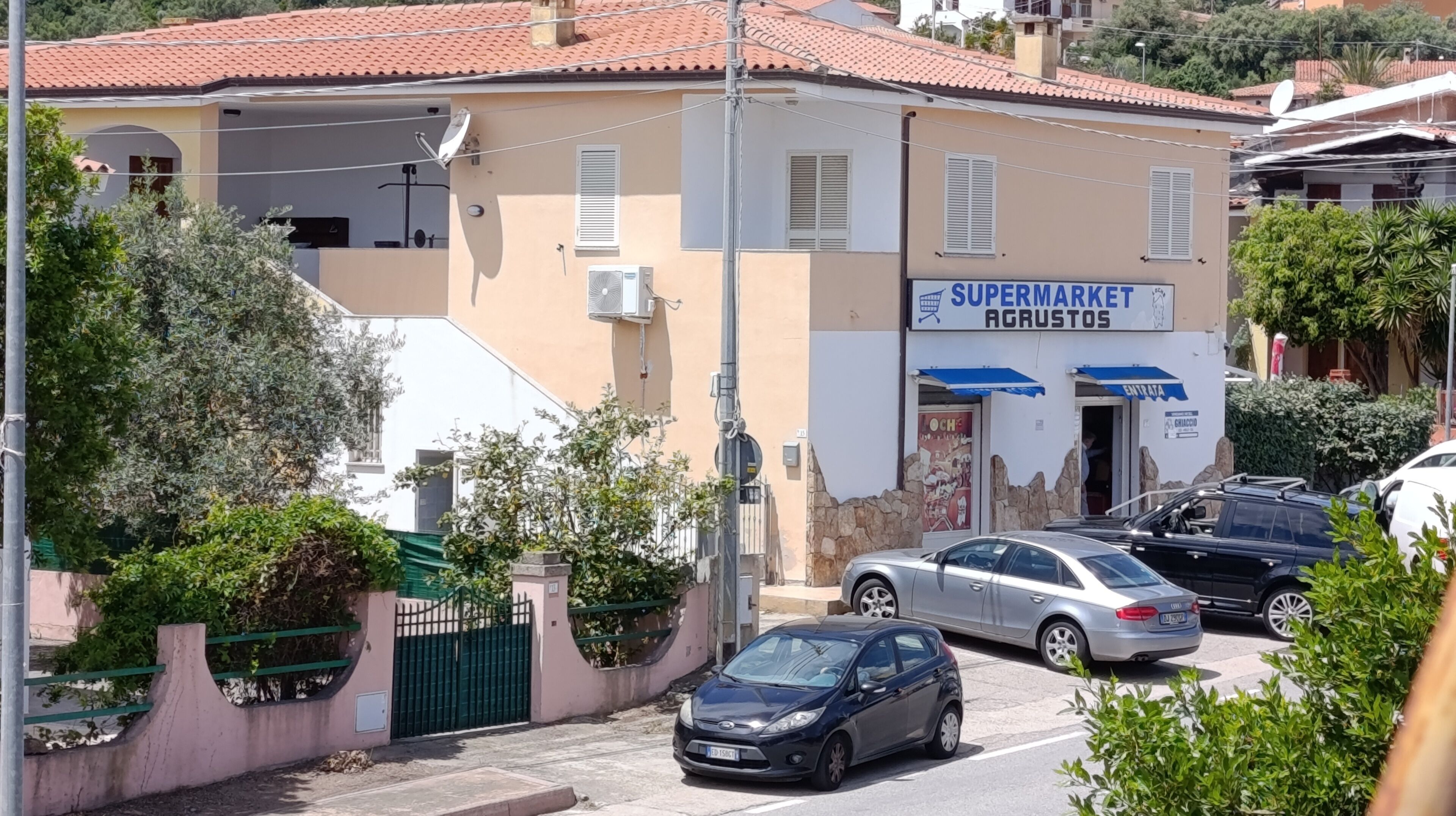 Un edificio con un cartello che recita 'SUPERMARKET AGRUSTOS' e un ingresso chiuso da cancello.