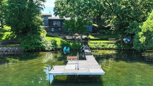 A wooden dock extending into a calm body of water, surrounded by lush greenery and a residential building in the background. - 4 Bedroom cabin featuring breathtaking views and clean water just steps away! (Alexandria)