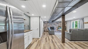 A modern kitchen with a stainless steel refrigerator, wooden flooring, a stone wall, a gray armchair, and a gray sofa. - 4 Bedroom cabin featuring breathtaking views and clean water just steps away! (Alexandria)