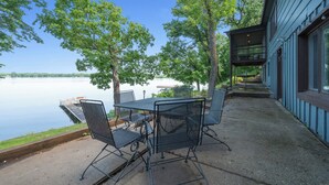 An outdoor patio with a table and chairs overlooking a lake, a dock, and a building with large windows. - 4 Bedroom cabin featuring breathtaking views and clean water just steps away! (Alexandria)