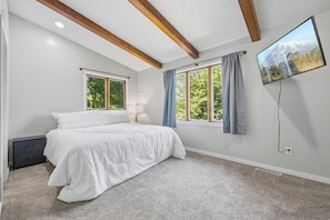 A bedroom with a bed, two windows, a TV, and a nightstand.