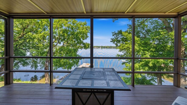 A covered outdoor area with a table and chairs, large windows offering a view of trees and a body of water. - 4 Bedroom cabin featuring breathtaking views and clean water just steps away! (Alexandria)