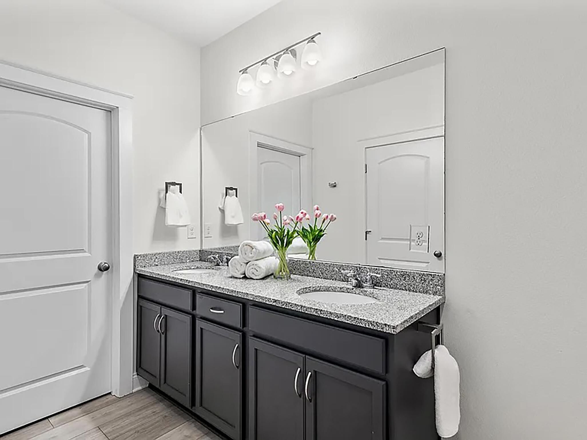 A bathroom with a large mirror, two sinks, dark cabinets, and a towel rack.