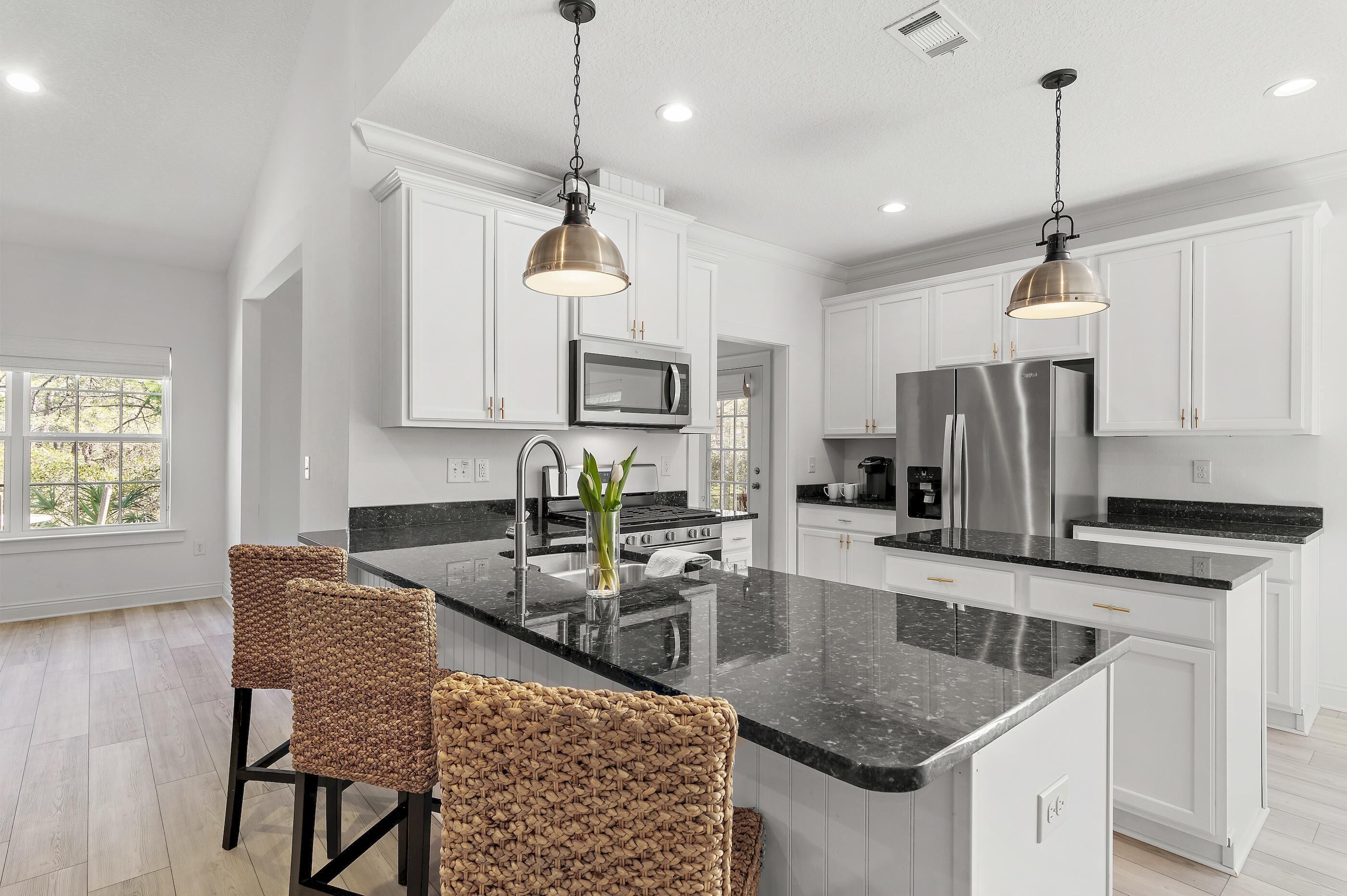 A modern kitchen with white cabinetry, stainless steel appliances, and a central island with bar stools.