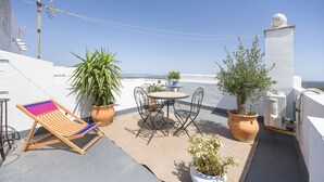 En tagterrasse med et bord, stole, krukker med planter og en liggestol.