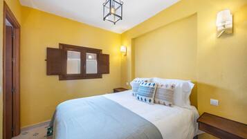 A bedroom with a bed, a window with shutters, a wall-mounted light, and a door.