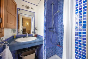 Casa de banho com chuveiro em azulejo azul, pia branca e espelho em cima.