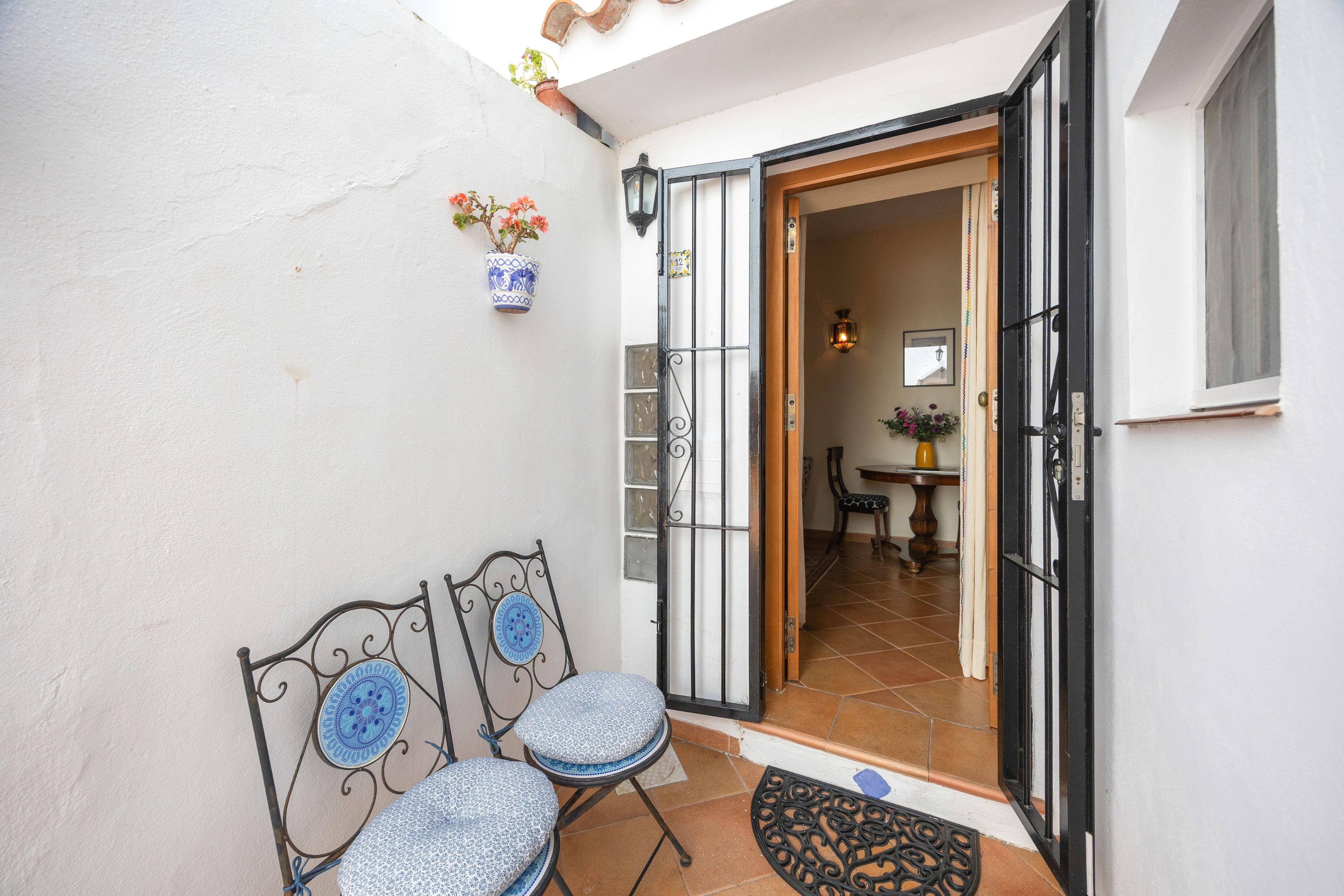 A patio area with two chairs and a small table, a door leading inside, and a potted plant on the wall.