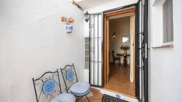 A patio area with two chairs and a small table, a door leading inside, and a potted plant on the wall.
