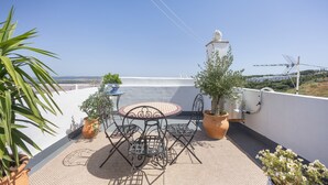 En tagterrasse med et bord og stole, plantekasser og udsigt over landskabet.
