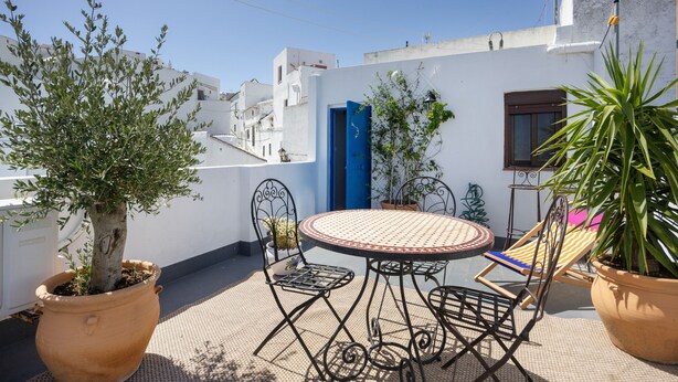 En terrasse med et rundt bord og stole, plantekasser og en blå dør.