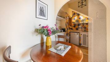 A dining area with a round wooden table, a yellow vase with flowers, and a framed picture on the wall.