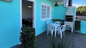 A turquoise building with a patio area featuring a grill, white plastic chairs, and a table. - Casa piscina praia da pinheira  (Palhoça)