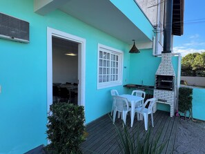 A turquoise building with a patio area featuring a grill, white plastic chairs, and a table.
