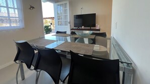 A dining area with a glass table, black chairs, a TV, and a door leading outside. - Casa piscina praia da pinheira  (Palhoça)