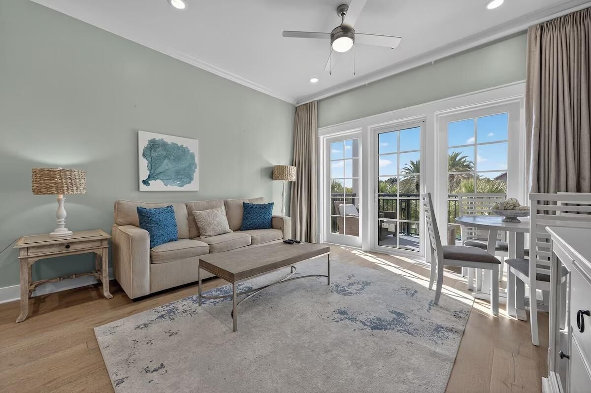 A living room with a sofa, coffee table, and a view of the outdoors through large windows.