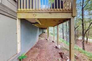 Eine Holzterrasse mit Geländer, gestützt von Säulen, führt zu einem Gebäude mit einer grauen Außenwand.