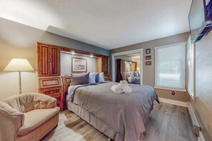 Ein Schlafzimmer mit einem Bett, einem Sessel, einer Lampe, Holzschränken und einem Fenster.