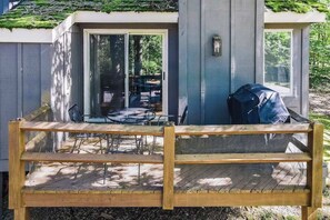 Eine Holzterrasse mit überdachtem Grillbereich, einem Esstisch mit Stühlen und einem überdachten Patio-Tisch.
