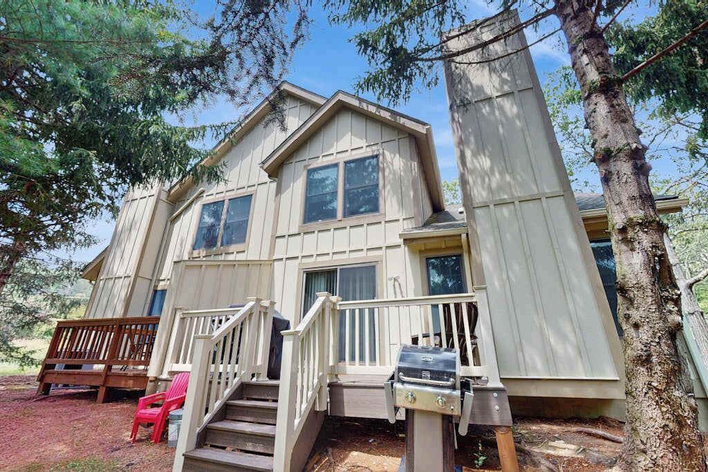 A two-story cabin with a front porch, a grill, and a red chair.