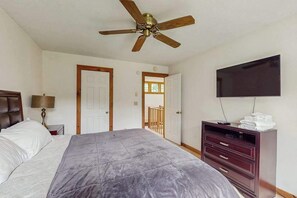 Ein Schlafzimmer mit einem Bett, einem Deckenventilator, einem Fernseher, einer Kommode und einer Tür zu einem anderen Raum.