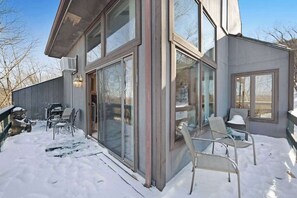 Ein modernes Haus mit großen Glasfenstern, einer überdachten Terrasse mit Stühlen und verschneitem Grund.