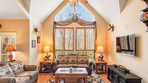 Ein gemütliches Wohnzimmer mit hoher Decke, Kamin und großem Fenster.