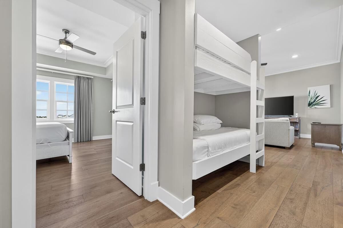 A modern hotel room with a bunk bed, a desk, a chair, a television, and a ceiling fan.