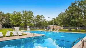 A swimming pool with lounge chairs, a lifeguard tower, and a fenced area with trees.