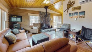 A cozy cabin interior with a stone fireplace, leather furniture, and a television.