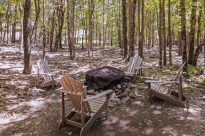 A campsite with four wooden chairs arranged around a central fire pit, surrounded by trees. - Woodland Cabin with Firepit, Pools & Lake Beach (Albrightsville)