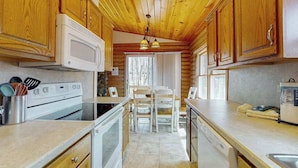 A kitchen with wooden cabinets, a microwave, stove, and a dining area with chairs and a table.
