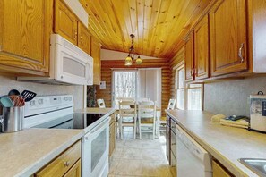 A kitchen with wooden cabinets, a microwave, stove, and a dining area with chairs and a table. - Woodland Cabin with Firepit, Pools & Lake Beach (Albrightsville)