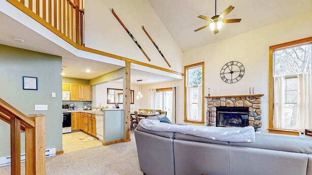 A spacious living area with a stone fireplace, a large gray sectional sofa, a wooden coffee table, and a kitchen in the background. - FIREPLACE - 3BR Townhouse - Near Camelback Ski (Tannersville)