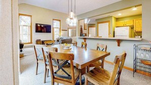 A dining area with a wooden table and chairs, a TV mounted on the wall, and a kitchen area with cabinets and a refrigerator. - FIREPLACE - 3BR Townhouse - Near Camelback Ski (Tannersville)