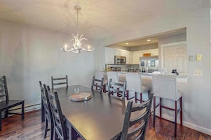 A dining area with a wooden table and chairs, a chandelier, and a kitchen in the background. - Gorgeous Townhouse with Fireplace Near Camelback (Tannersville)