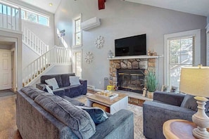 A living room with a stone fireplace, a TV mounted above it, and a staircase leading to another level. - Gorgeous Townhouse with Fireplace Near Camelback (Tannersville)