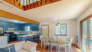 A spacious living area with a sofa, dining table, and chairs, a kitchen with blue cabinets, and a large window.