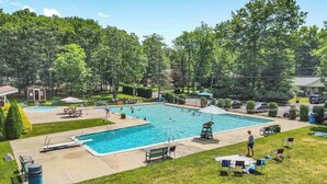 A swimming pool with a diving board, surrounded by grass and trees.