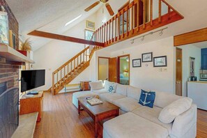 Ein geräumiges Wohnzimmer mit einer Holztreppe, einem Kamin, einem Fernseher und einem großen Sofa.