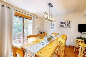 Ein Essbereich mit Holztisch, Stühlen, einer Chandelierleuchtre, einem Motivationsschild und einem Fernseher.