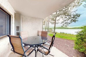 Une terrasse couverte avec une table ronde et quatre chaises, donnant sur un lac et une végétation luxuriante.