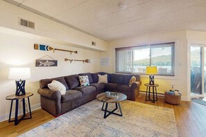 A living room with a brown sectional sofa, a round coffee table, a lamp, and a window with blinds. - Cozy Lakefront Oasis with Fireplace (Lake Harmony)