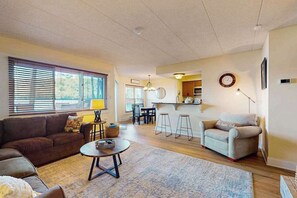 A living room with a sofa, a coffee table, and a dining area with a bar. - Cozy Lakefront Oasis with Fireplace (Lake Harmony)