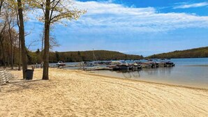 Ein sandiger Strand mit Booten an einem Steg, Bäumen und einem ruhigen See.